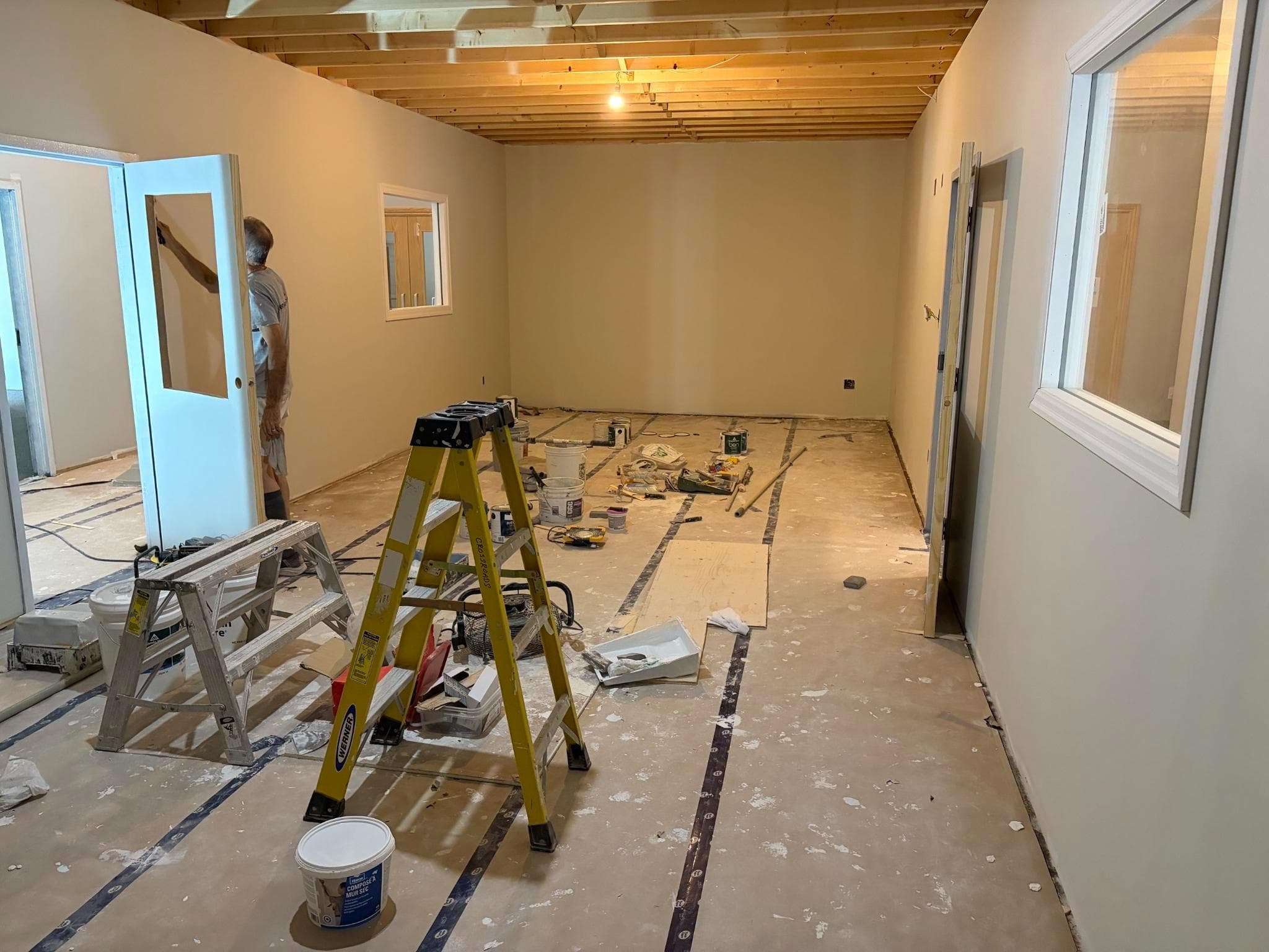 A classroom under construction, with open joists, a ladder and paint supplies